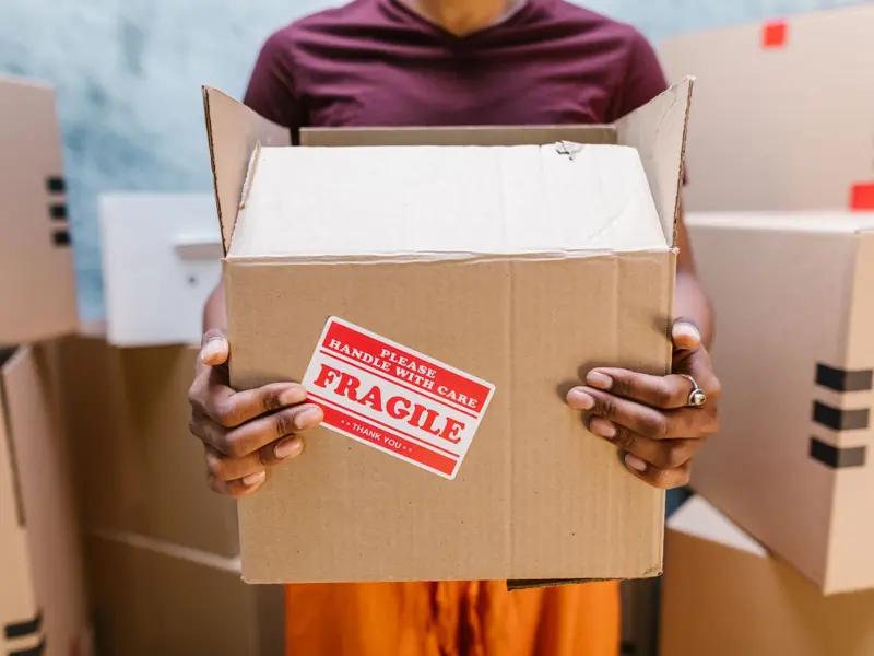 A person holding a cardboard box labeled 'Fragile' during a moving process indoors.