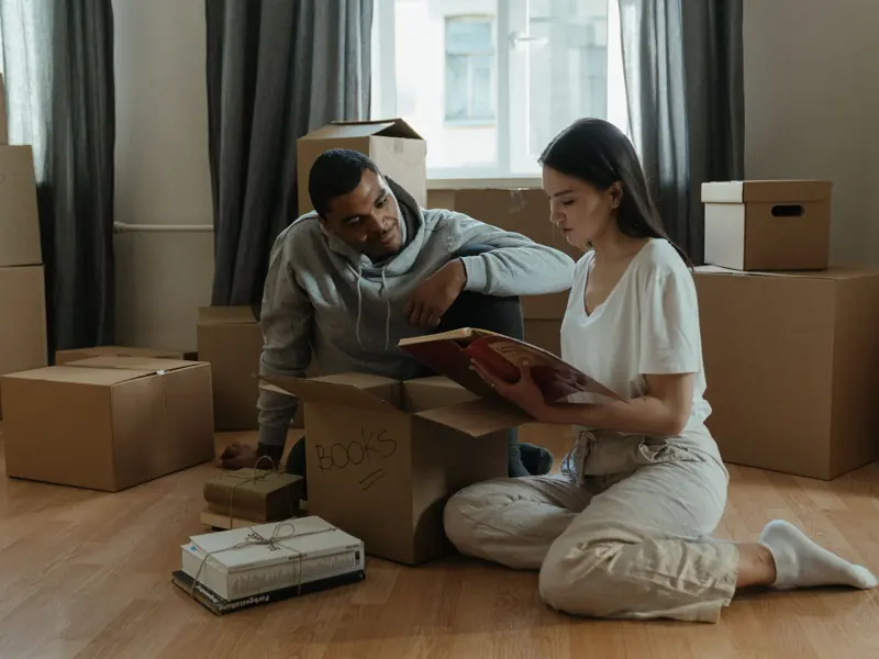 A couple unpacking boxes and reminiscing over a photo album in their new apartment.