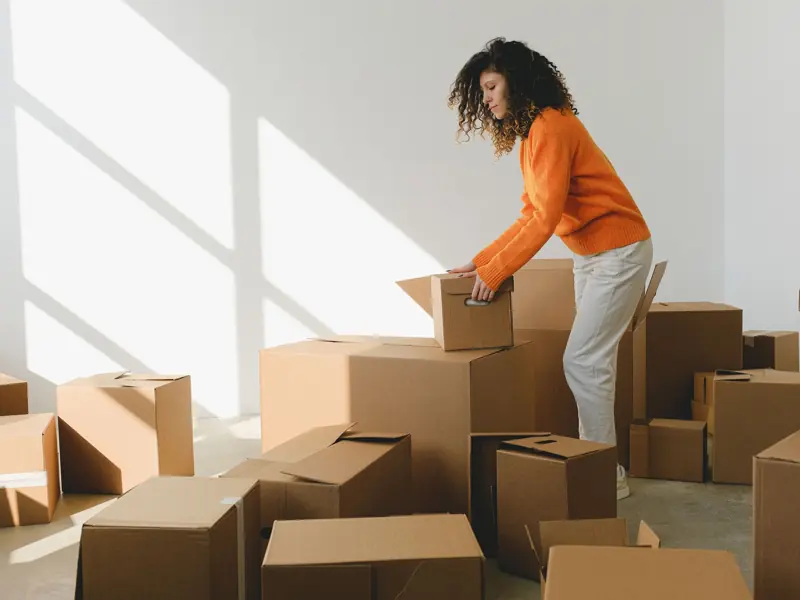 Side view of concentrated young lady with curly hair in casual clothes packing and arranging cardboard boxes while preparing for moving into new apartment in daylight