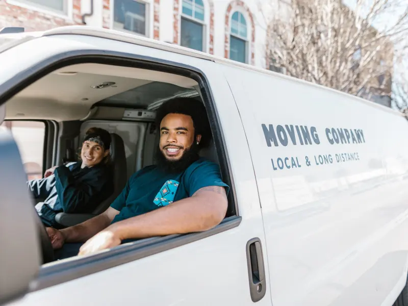 Two movers smiling from their moving company van parked on a sunny day.