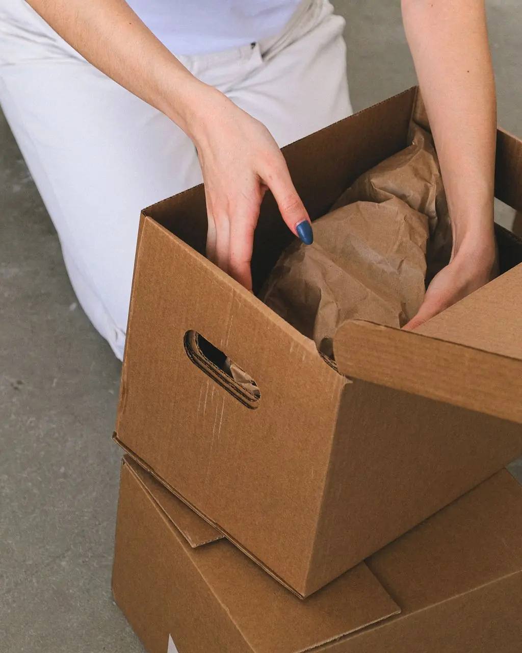 From above of crop anonymous relocating female packing wrapped items into carton box while preparing for moving to new apartment