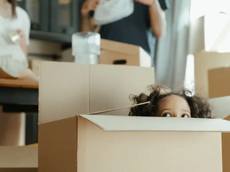 A child peeks out of a cardboard box while moving into a new home, capturing a playful moment.