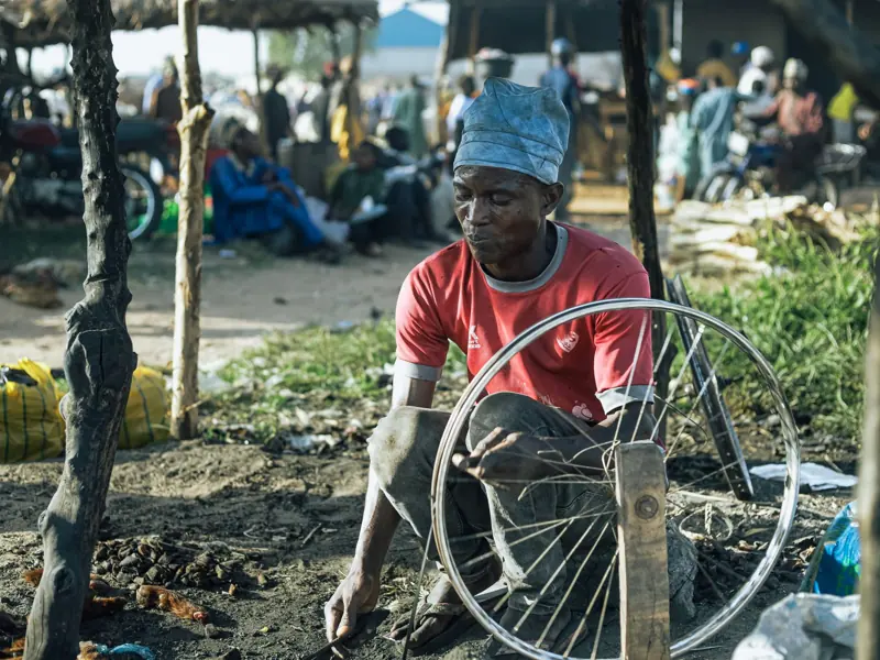 A man repairs a bicycle wheel at an outdoor market, showcasing local craftsmanship.