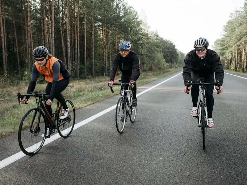 Three cyclists are enjoying a ride on a scenic forest road during the day.