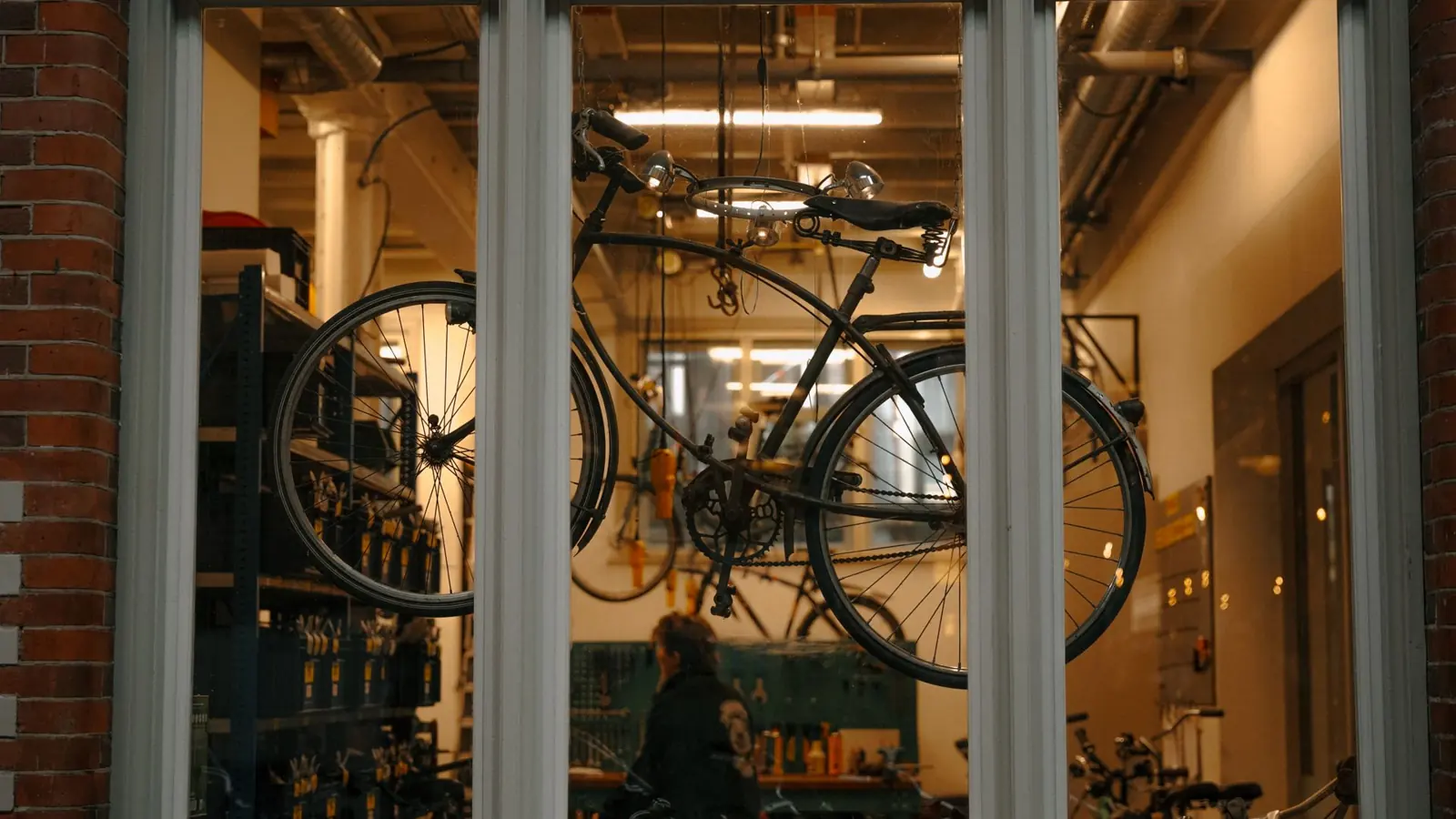 A cozy bicycle workshop in Amsterdam viewed through a window with bicycles hanging inside.