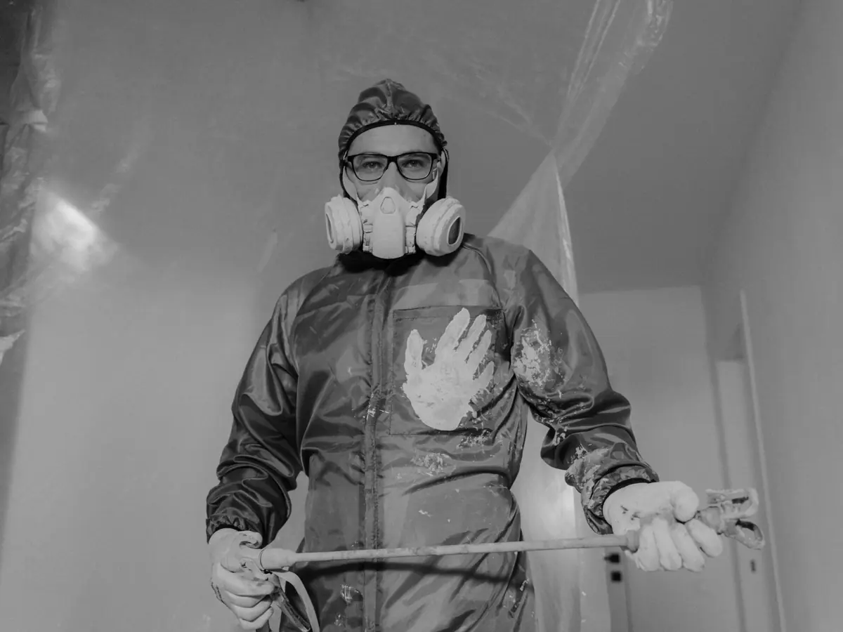 A worker in protective gear painting indoors during a home renovation project.