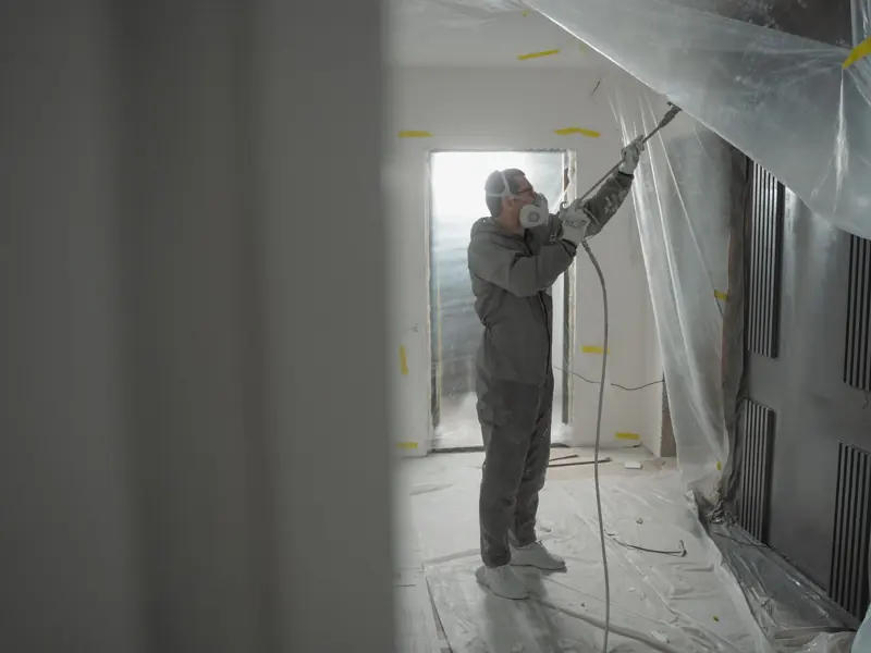 Man in protective gear spray painting a house's interior during renovation work.