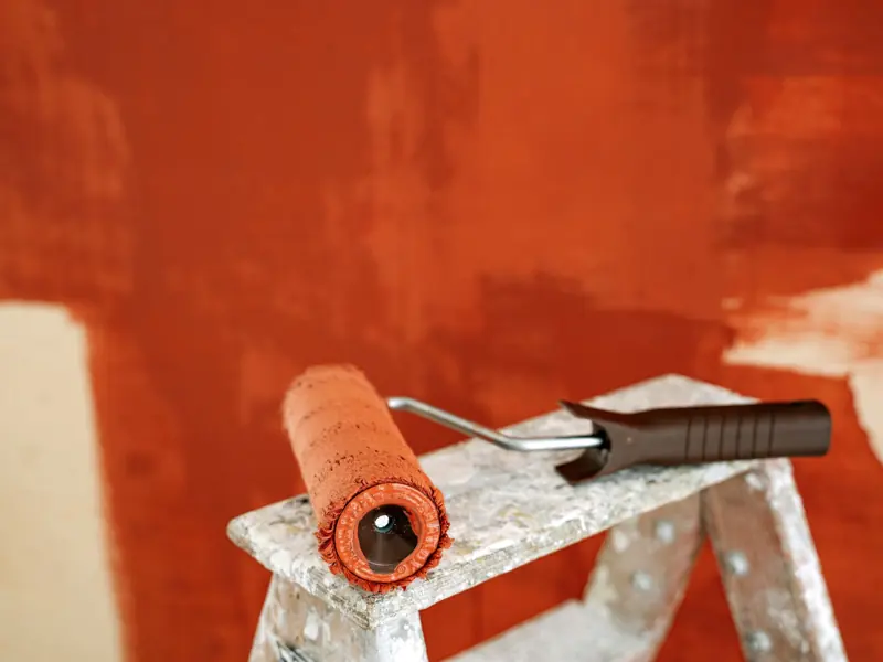 Close-up of a paint roller resting on a stepladder against a partially painted wall.