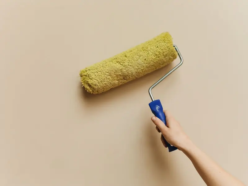 A hand using a yellow paint roller to paint a beige wall. Perfect for DIY and home improvement themes.