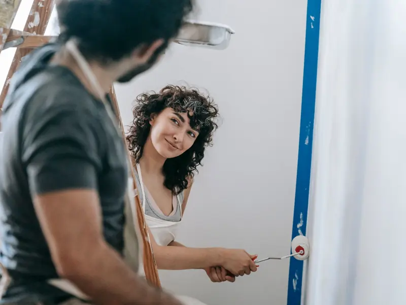 A happy couple painting walls together in their home, enjoying a playful moment during renovation.