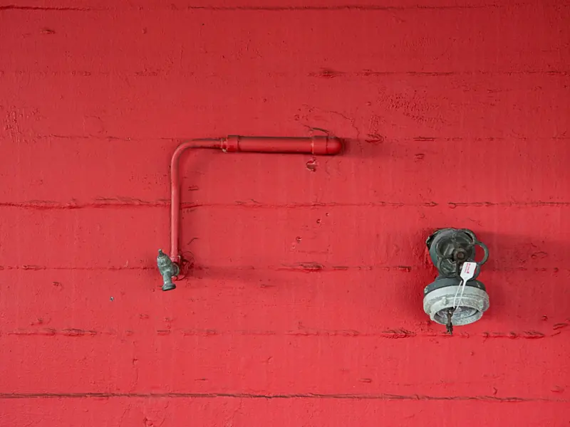 Close-up of a red wall featuring an industrial faucet and pipeline. Minimalist design.