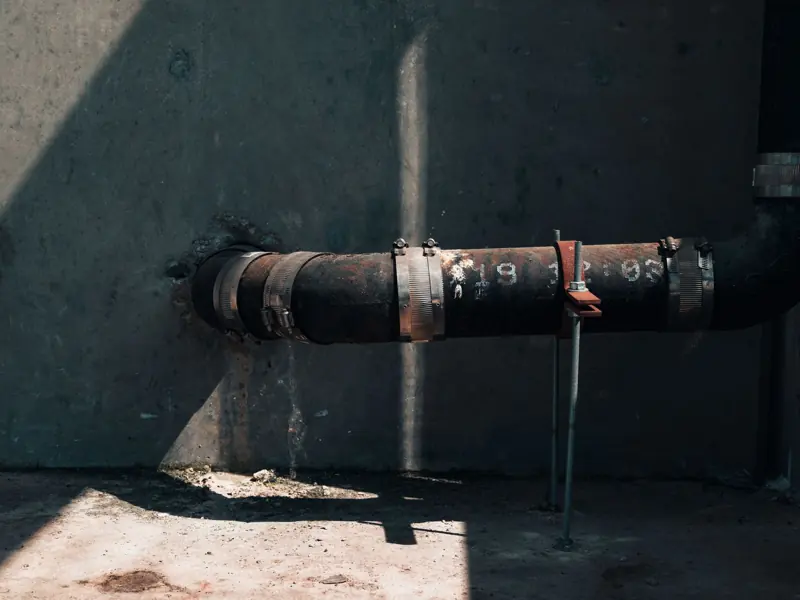 Rusted industrial pipe on a concrete wall with dramatic sunlight and shadows, showcasing urban decay.