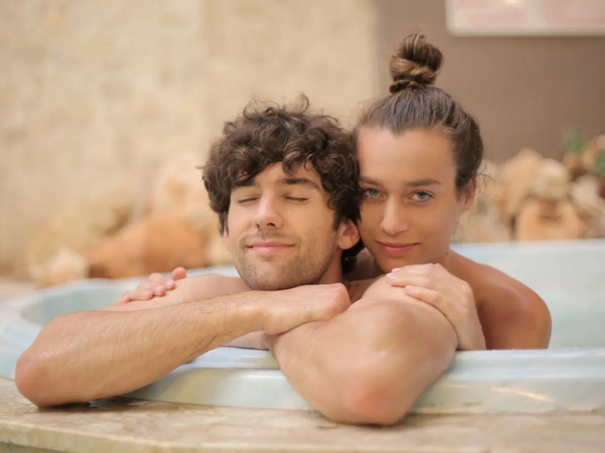 Young cheerful man and woman taking bath together enjoying holidays on blurred background of spa resort with marble interior and having romantic moments