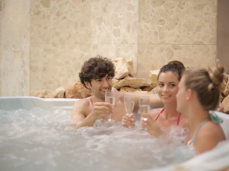 Group of friends toasting with drinks in a hot tub, enjoying relaxation and togetherness indoors.