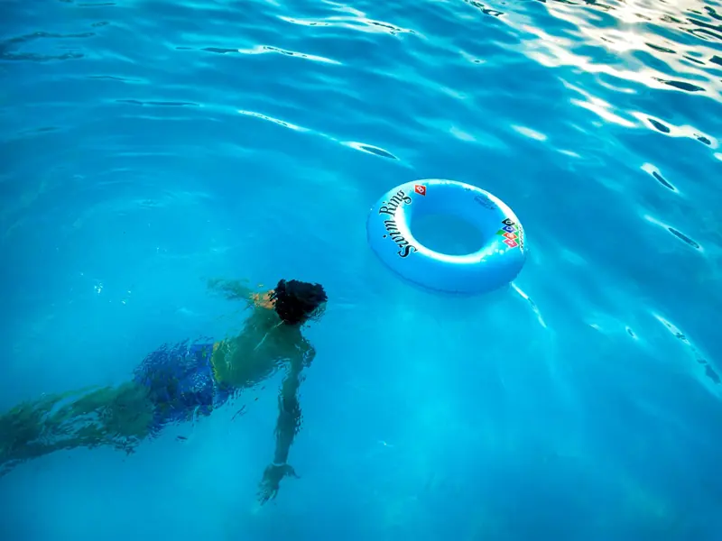 An individual swims underwater in a bright pool beside a floating swim ring.