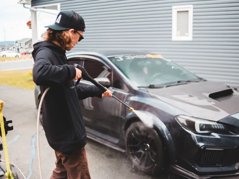 Back view of faceless worker using hosepipe while washing expensive black luxury sports car in daytime