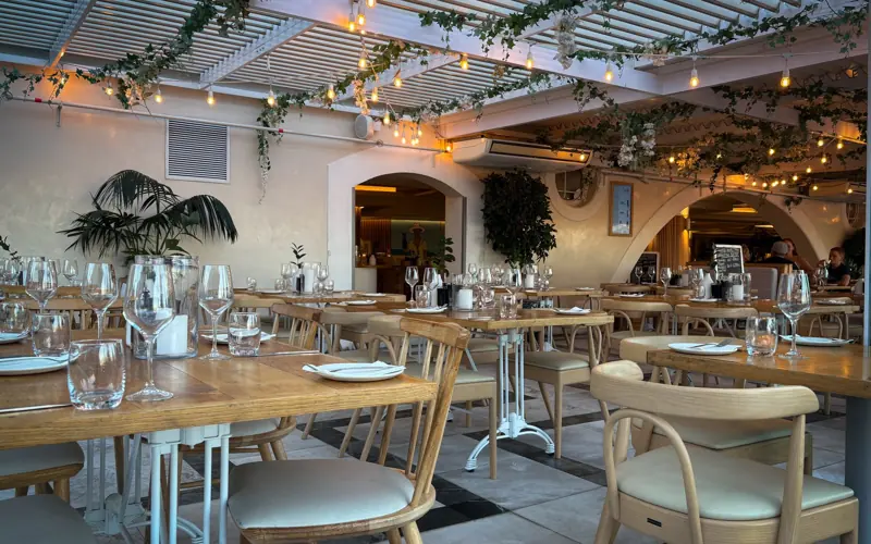 Elegant indoor restaurant setting with wooden furniture, warm lighting, and decorative foliage.