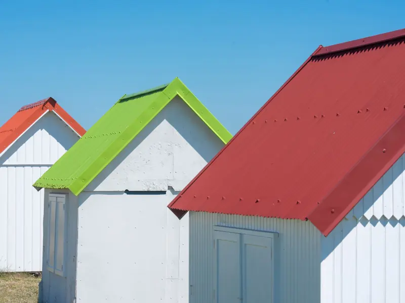 White beach huts with bright red, green, and orange rooftops under a clear blue sky.