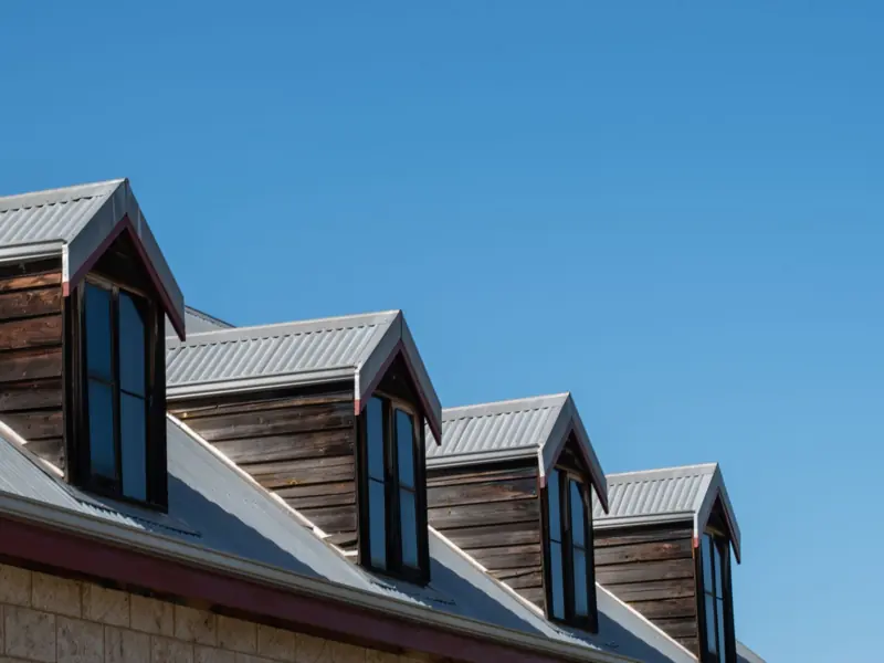 Modern triangular rooftops with windows against a clear blue sky.