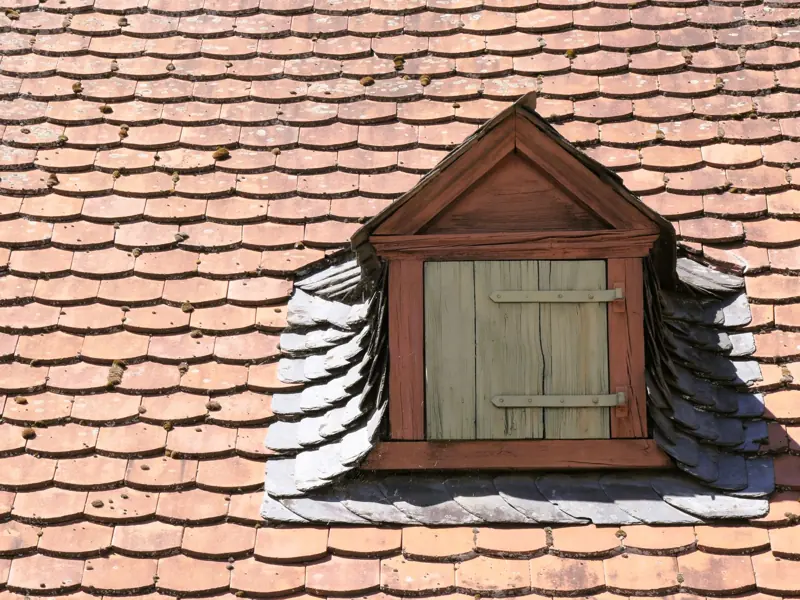 Charming dormer window on a vintage shingled roof, offering an architectural close-up.