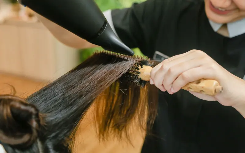 Close-up of hair stylist using a hairdryer and brush to style long hair.