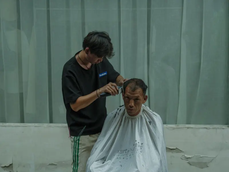 A hairdresser cuts a man's hair under natural lighting, creating a casual and relaxed atmosphere.