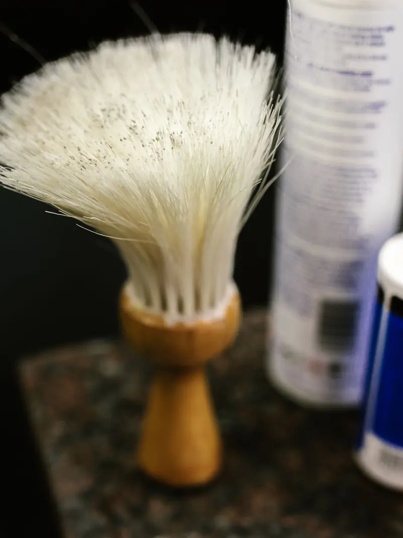 Close-up of a wooden handle barber neck duster in a barbershop setting.
