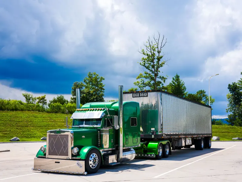 A striking green semi-truck parked outdoors with a dramatic cloudy sky backdrop.