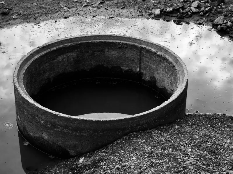 Circular concrete structure in puddle reflects sky in monochrome.