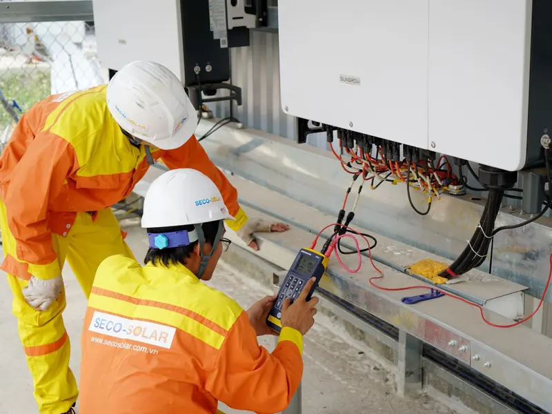 Two electrical engineers installing and testing solar power systems wearing safety gear at a construction site.
