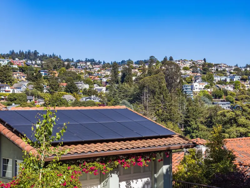 Solar panels on a suburban home, surrounded by lush greenery and a sunny blue sky.