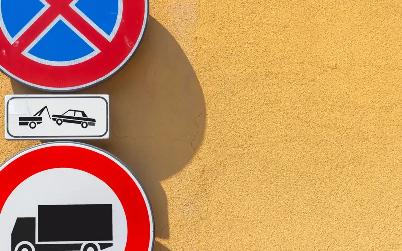 Traffic signs against a bright yellow wall; no parking and truck prohibition displayed.