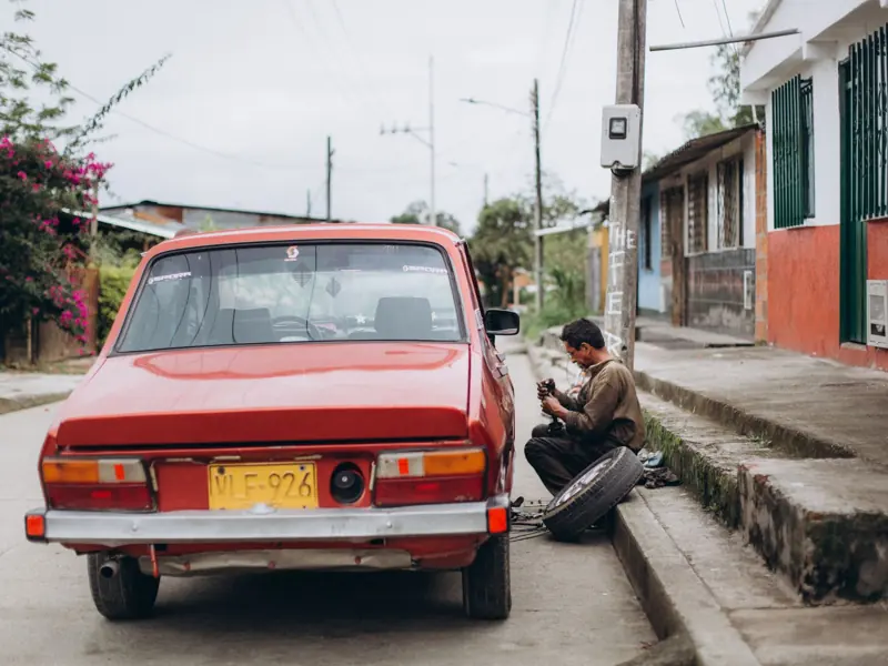 Mechanic repairing a red car on a street side in an urban neighborhood. Manual work in action.