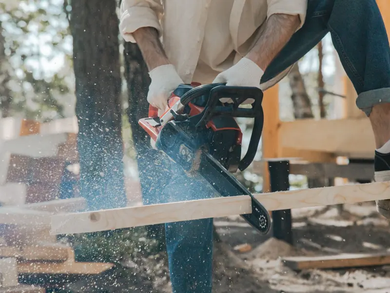 Outdoor scene of a man skillfully using a chainsaw on wood, showcasing carpentry expertise.
