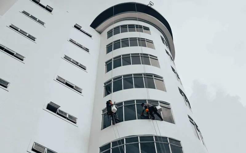 Workers cleaning windows on a modern high-rise building using ropes. Urban architectural maintenance.