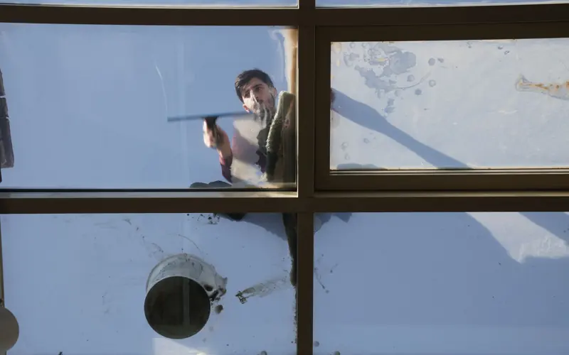 A male window cleaner washing the exterior glass roof from above with a tool during daylight.