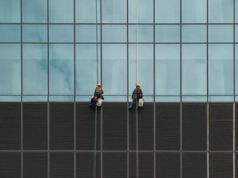 Two window cleaners suspended on ropes cleaning a modern skyscraper facade.