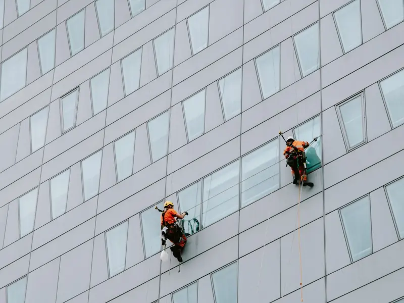 High-rise window washers in safety gear cleaning a skyscraper facade.