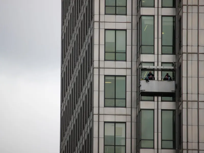Two workers cleaning windows on a high-rise building facade in an urban environment.
